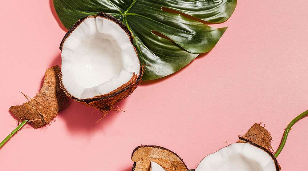aufgeschnittene Kokosnuss und Blatt vor rosa Hintergrund